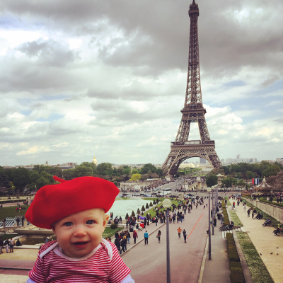 A baby in a red beret poses with the famous Eiffel Tower in the distance