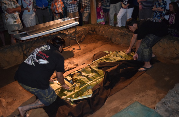  Two men lift food from a traditional earth oven at Kilohana Estate and Plantation on the Hawaiian Island of Kauai.