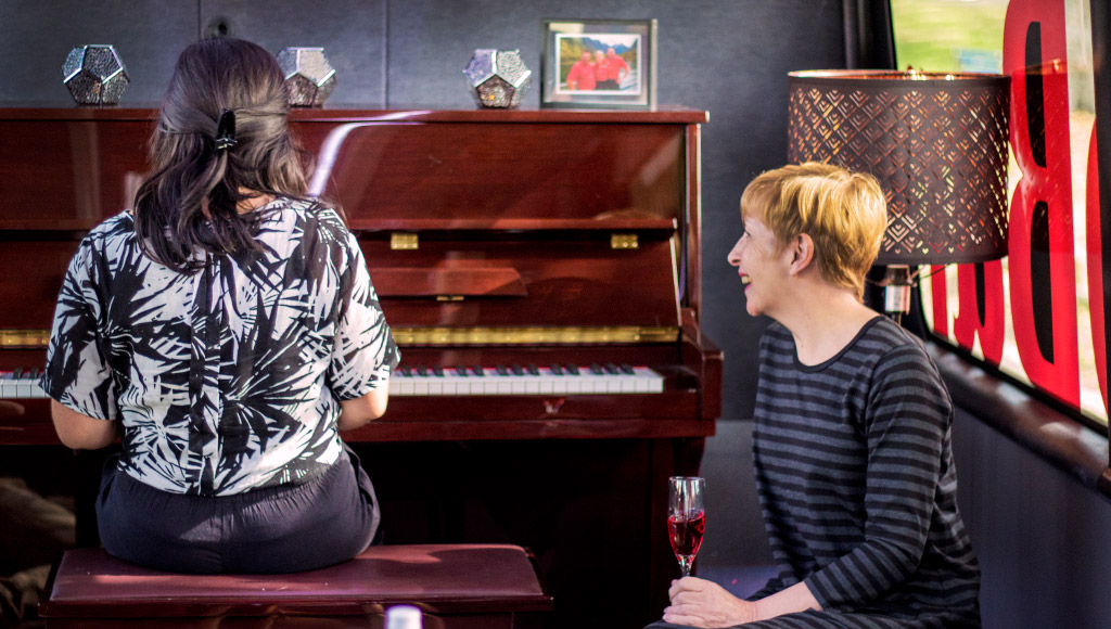 A woman enjoys a beverage while listening to a pianist on the bus.